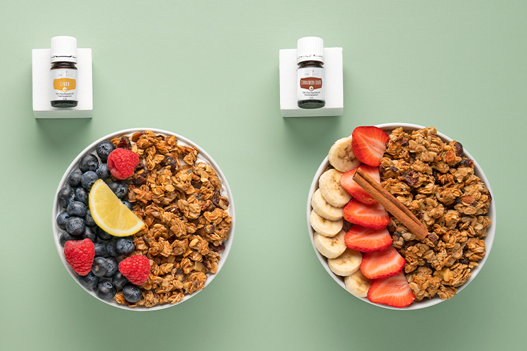 Lemon+ and Cinnamon Bark+ essential oils with bowls of granola and fruit