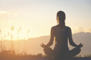 Žena meditující při západu slunce