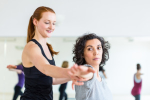 Инструктор помогает женщине принять позу йоги во время занятия