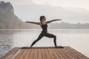 Mujer practicando yoga mirando hacia el agua al final de un muelle