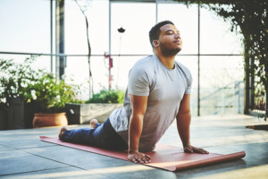 Hombre haciendo yoga rodeado de plantas y ventanas