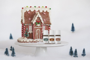 Frascos dos óleos essenciais de Cinnamon Bark+, Ginger+ e Peppermint+ com uma casa de biscoitos de gengibre de Natal