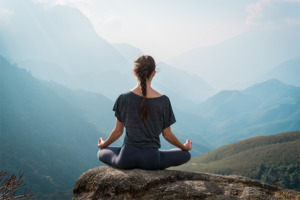 Žena praktikující jógu, meditaci a manifestaci na úpatí hory