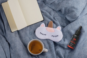 Nature's Ultra Cinnamon CBD Öl auf Bett mit Einhorn-Schlafmaske, einer Tasse Tee und Tagebuch