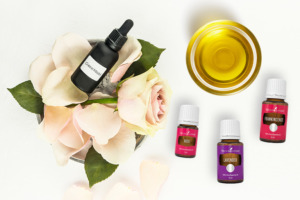 Schale mit Öl, frische Rosen, Pipettenfläschchen mit Gesichtsöl Aufschrift und ätherisches Lavendelöl, Rosenöl und Weihrauchöl