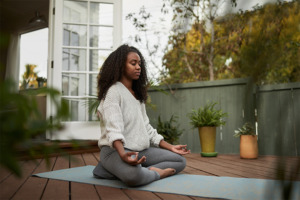 Meditierende Frau im Schneidersitz auf Yogamatte auf Terasse mit entspanntem Gesichtsausdruck