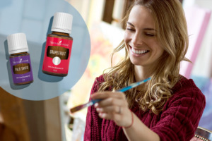 Glücklich aussehende Frau beim Malen mit Pinsel auf Leinwand und ätherisches Grapefruitöl und Palo Santo