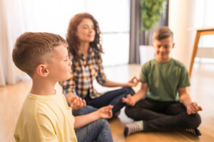 Mutter mit ihren zwei Kindern beim Meditieren zu Hause