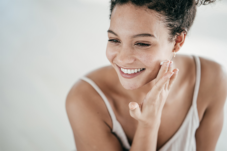 Hymyilevä nainen levittää ihonhoitotuotetta kasvoille
