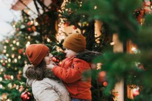 Weihnachtliche Atmosphäre und Mutter mit Kind auf dem Arm mit Weihnachtsbaum und Weihnachtslichtern im Hintergrund