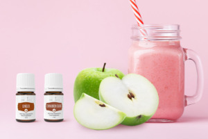 Batido rosa rodeado de manzanas verdes y los aceites esencials Ginger+ y Cinnamon Bark+.