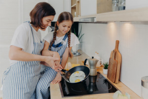 Afbeelding van een volwassene en kind die eieren koken in de keuken.