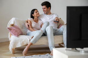 Image of a couple (man and woman) curled up on the sofa watching a movie.