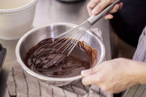 Afbeelding van iemand die in een kom met chocolade roert.