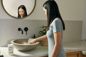 A képen egy nő tisztítja a fürdőszobai mosdót a Thieves® Kitchen & Bath Scrub segítségével.