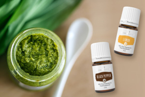 Ein Glas mit Bärlauchpesto mit Löffel, frischer Bärlauch und ätherisches Zitronenöl der Pluslinie sowie ätherisches Plusöl aus schwarzem Pfeffer von Young Living