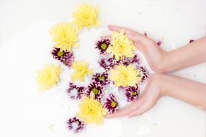 Image de mains dans un bain avec des pétales de fleurs.