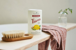 Obrázek čisticího prášku Thieves Kitchen & Bath Scrub na podnose s ručníkem a kartáčem na tělo.