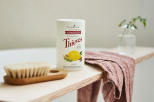 Bild von Thieves® Kitchen & Bath Scrub auf einem Baderegal mit Handtuch und Körperbürste.