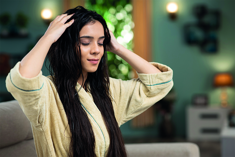 Kuva naisesta hieromassa öljyä hiuksiinsa.