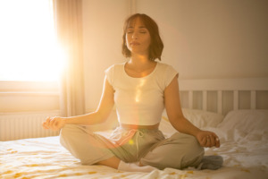 Bild på en kvinna som mediterar på sängen.