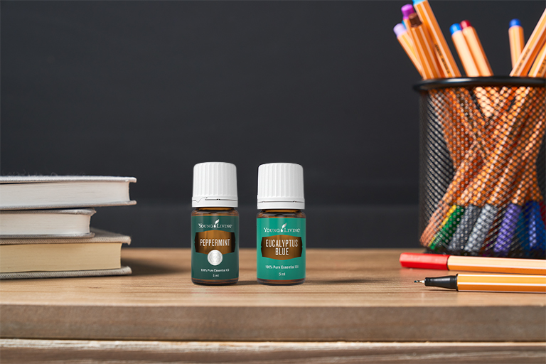 Image of Peppermint and Eucalyptus Blue essential oil placed on a desk with books and pens.