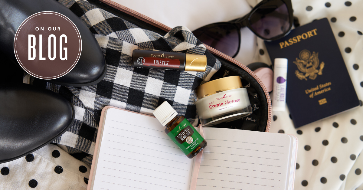 An open suitcase packed with clothes and essential oils for travel: Breathe again roll on, eucalyptus globulus essential oil, and ART creme masque