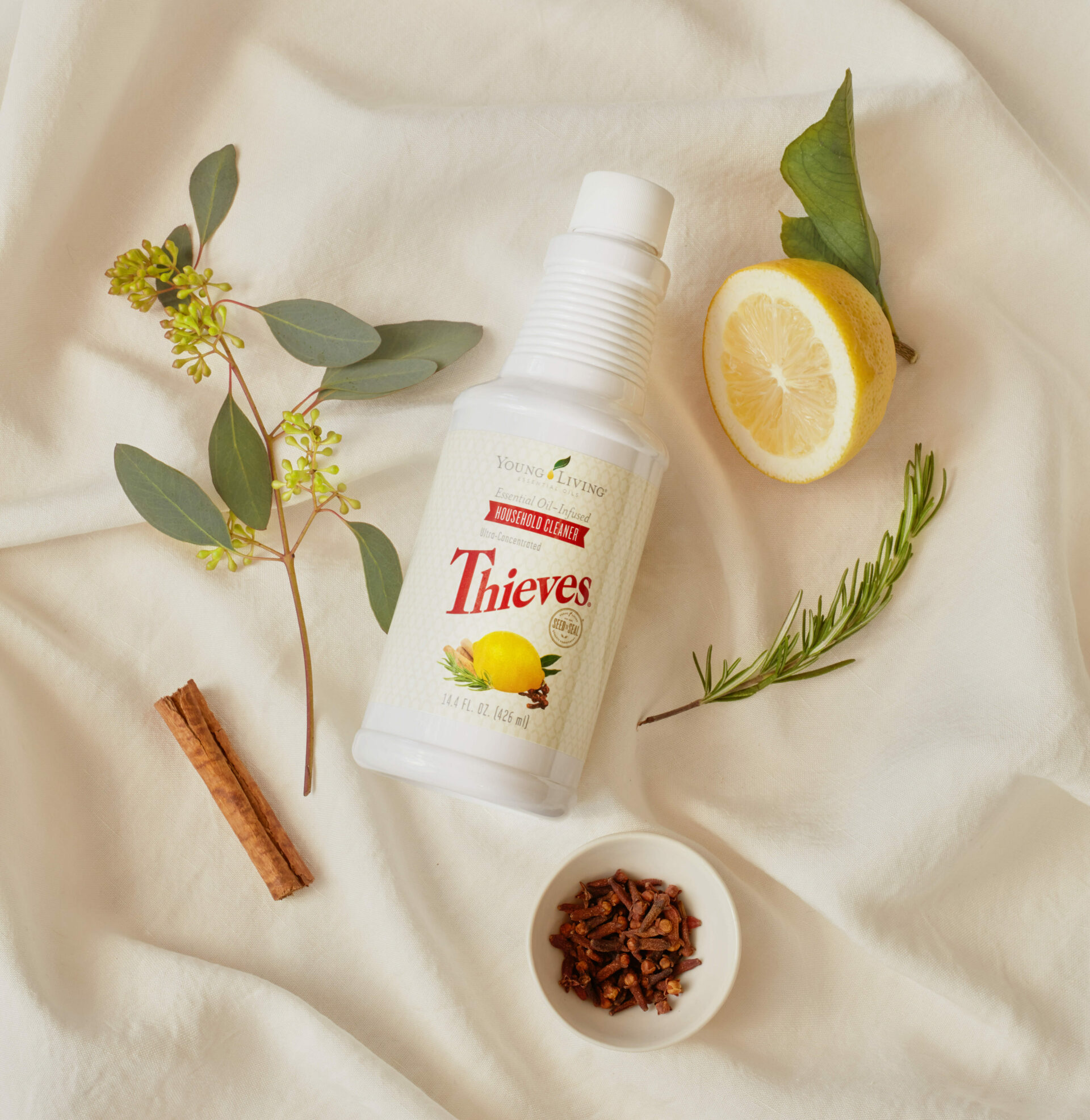 Thieves Household Cleaner sitting on a linen cloth next to botanicals, a lemon, cloves, and a cinnamon stick - Young Living Lavender Life Blog 