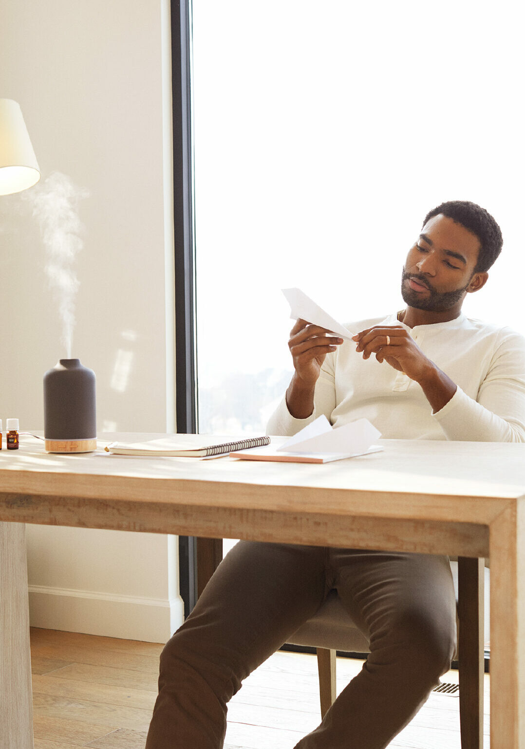 Man sitting at his desk making paper airplanes with Ember diffuser on - Young Living Lavender Life Blog 